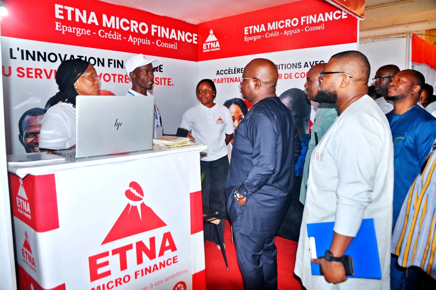 Eklin standing with a group of visitors at the ETNA Micro Finance stand