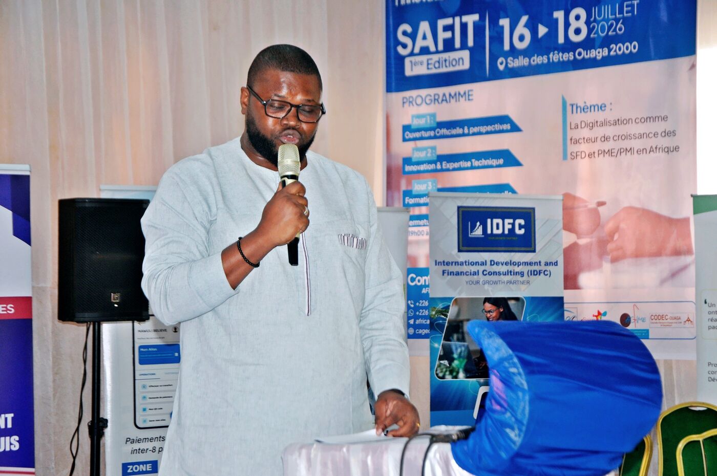 Eklin speaking with a microphone in front of the SAFIT 2026 banner, 1st edition, Ouaga 2000