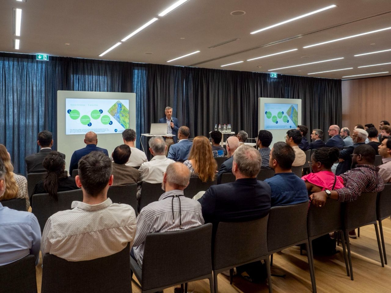 Audience in a conference room listening to a speaker presenting a slide titled Space Strategy, 4 priorities