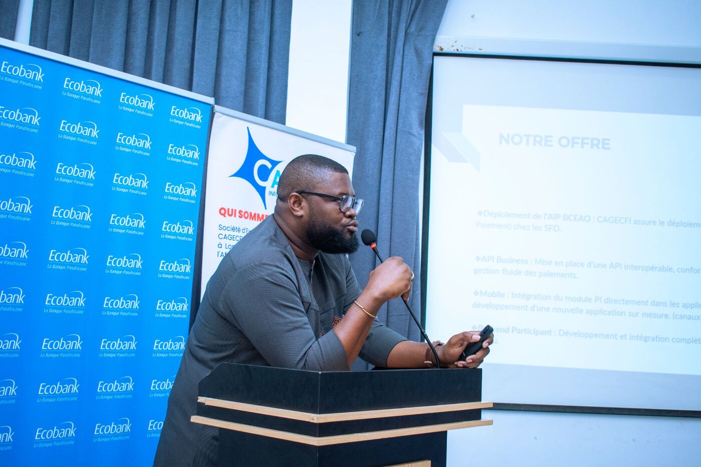 Eklin speaking at the lectern in front of a slide titled Notre offre, with Ecobank and CAGECFI banners